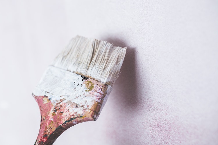 A picture of a paint brush held up against an unfinished wall
